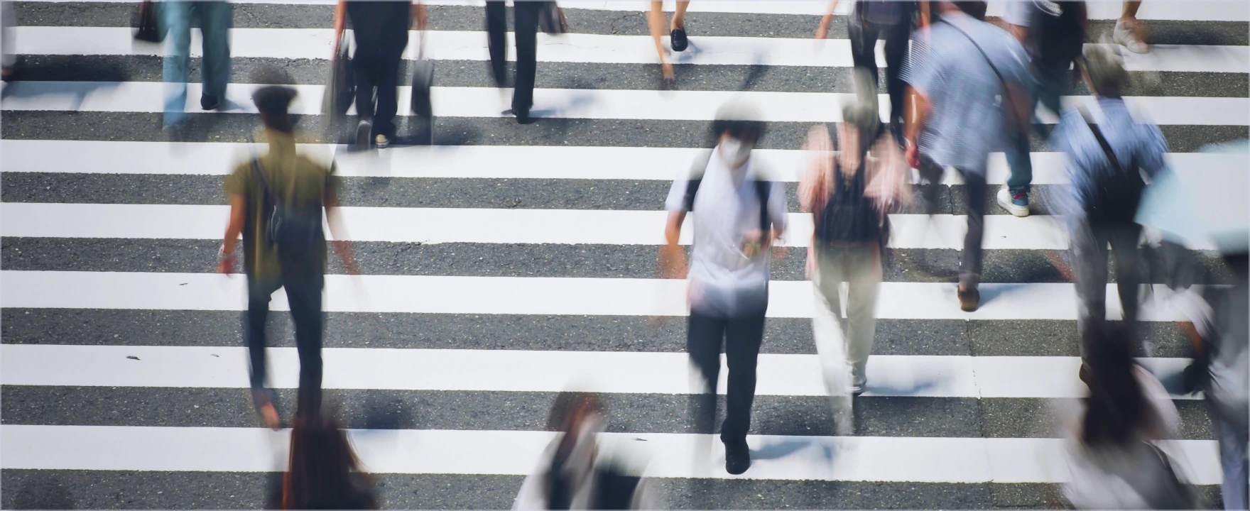 マスクを着用した大勢の人々が横断歩道を歩く様子。